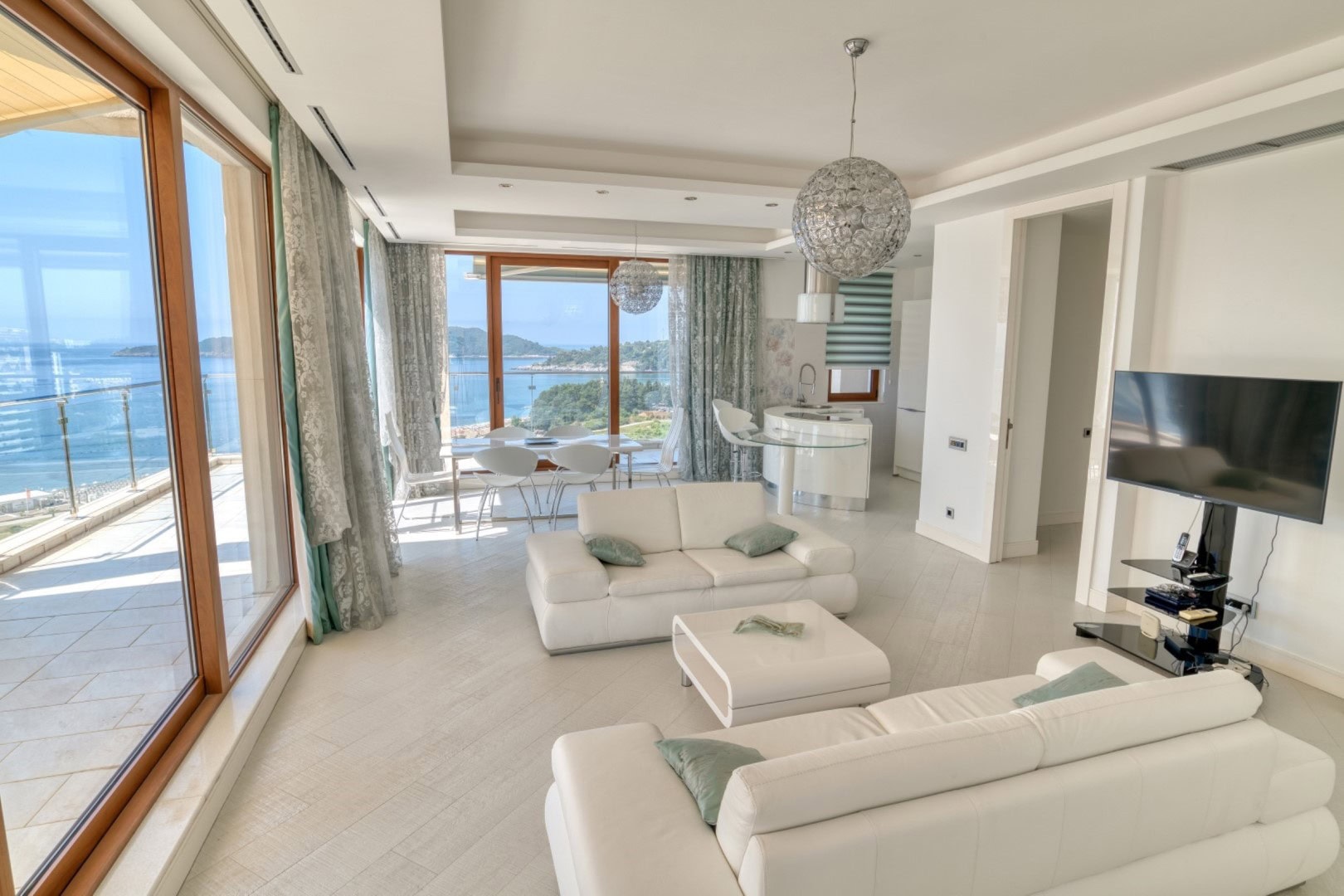 Living room in a penthouse in Bečići, Montenegro: white furniture, panoramic windows, and a direct view of the Adriatic Sea.