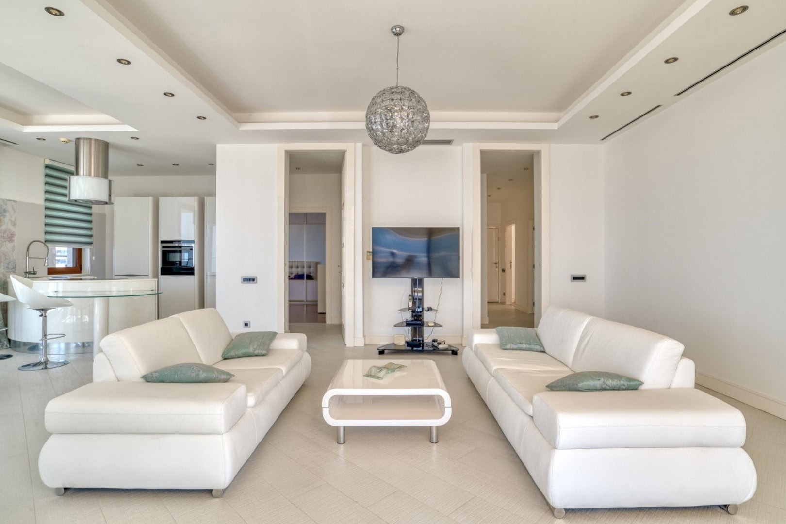 Modern living room with white sofas in a penthouse in Becici, Montenegro: stylish interior with a kitchen and TV.