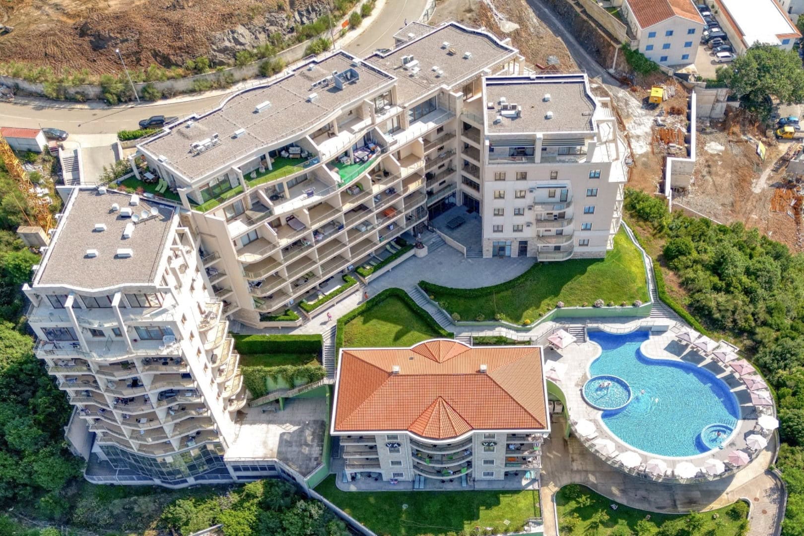 Aerial view of a residential complex with a swimming pool and terraces in Bečići, Montenegro: modern architecture and landscape.
