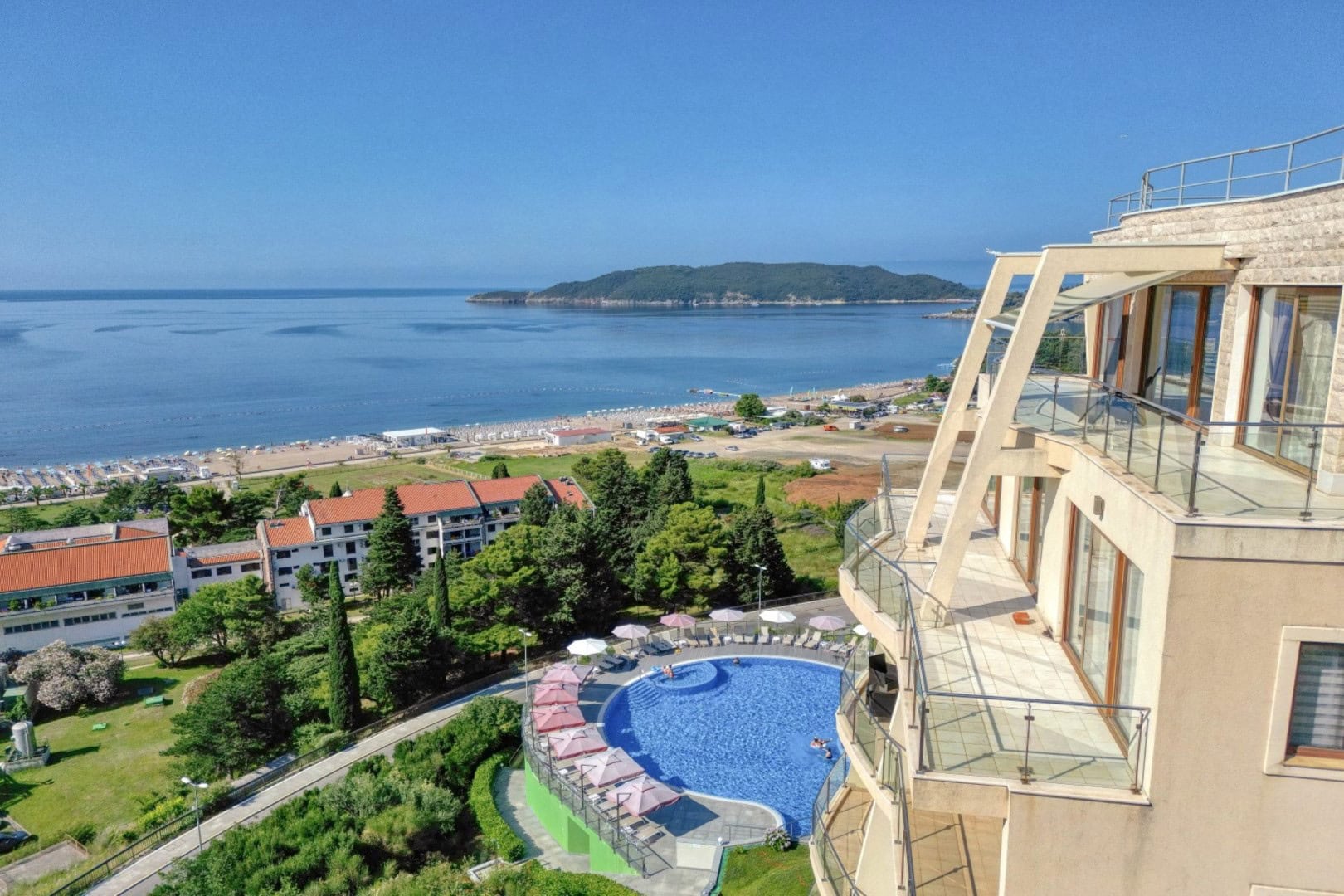 View from the penthouse terrace in Bečići, Montenegro: swimming pool, green park, and panoramic view of the sea and beach.