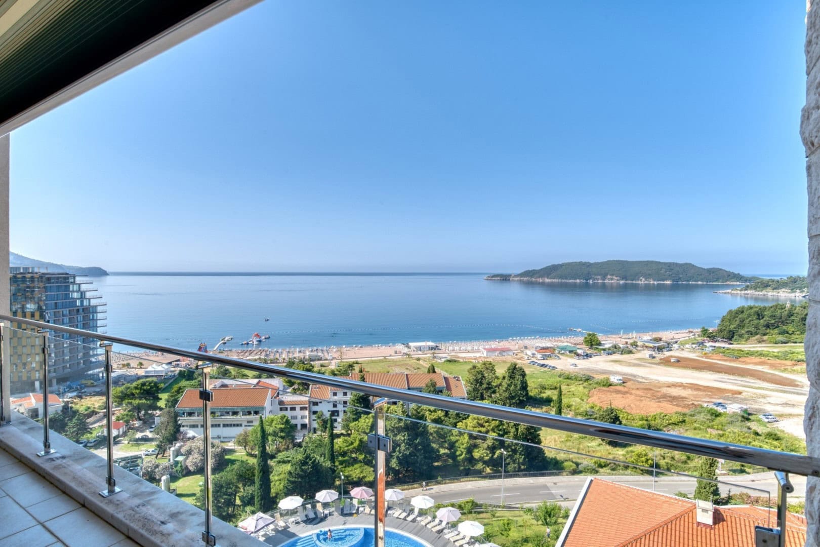 Panoramic view of the sea and Becici beach from a penthouse balcony in Montenegro, glass railing, view of the hotel and swimming pool.