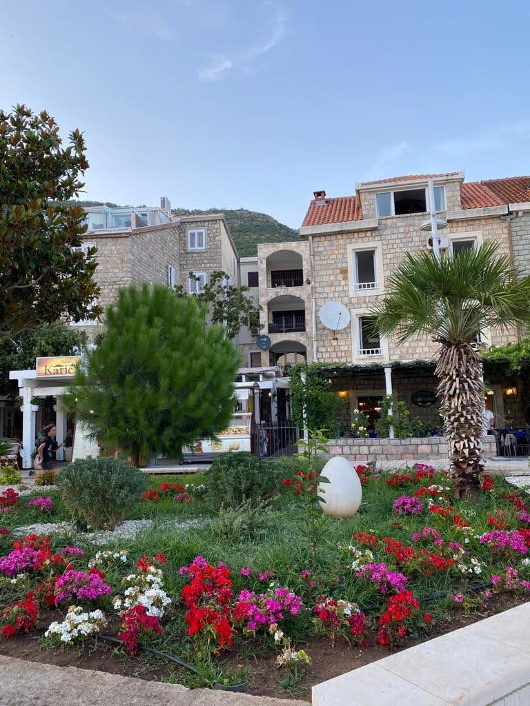 View of a stone residential complex with a blooming garden and a palm tree in Petrovac, Montenegro. Apartment in Petrovac No. 2128.