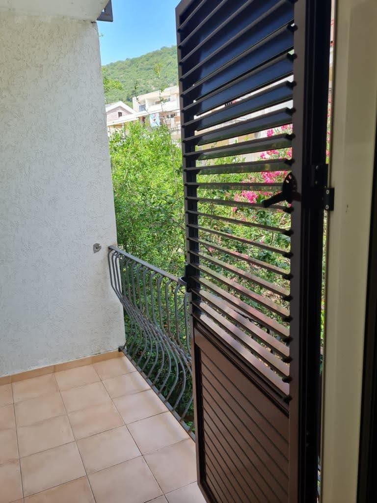 Balcony with wrought-iron railing and blinds in an apartment, Petrovac, Montenegro: view of green trees and mountains.