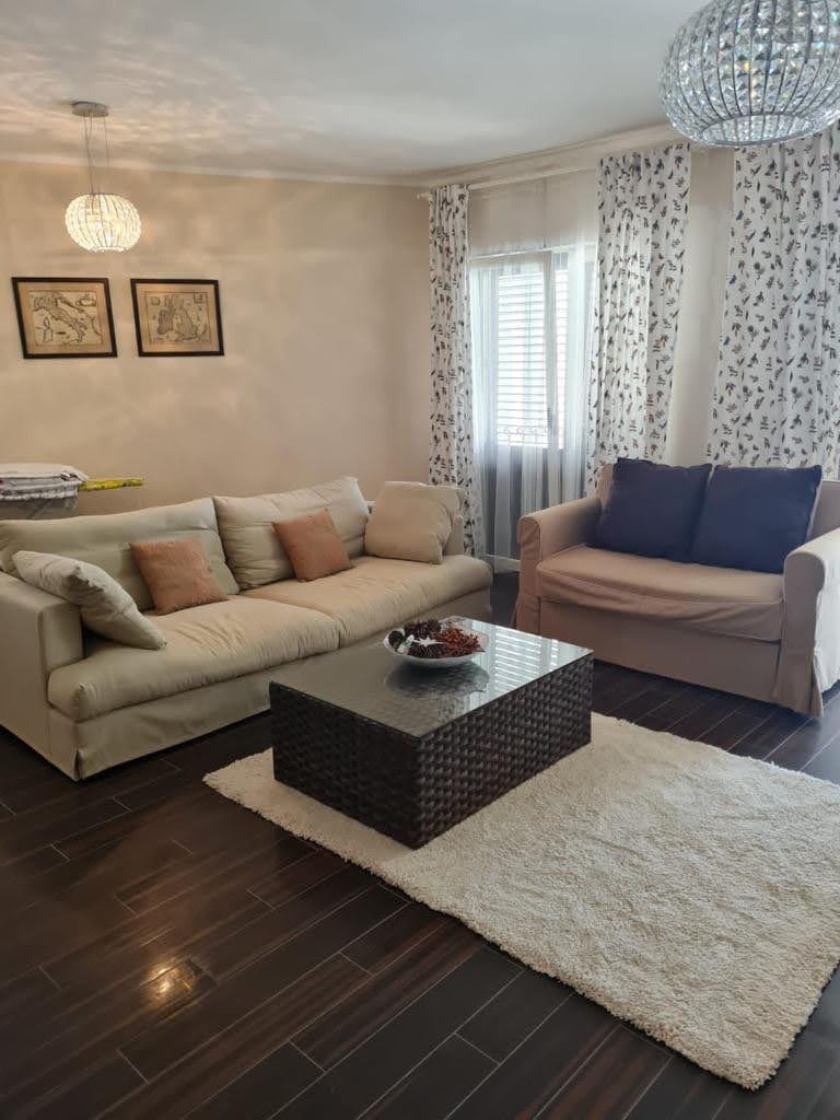 Cozy living room in an apartment in Petrovac, Montenegro: light sofas, a woven coffee table, and dark flooring.