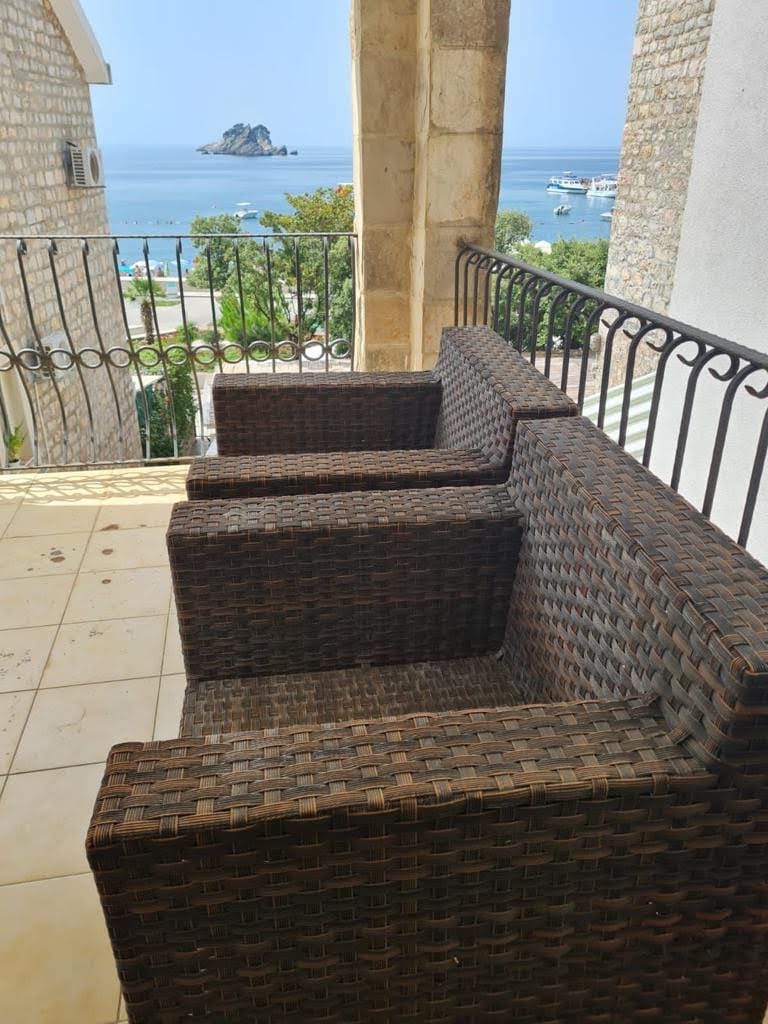 Balcony with wicker furniture and panoramic views of the sea and island in Petrovac, Montenegro.