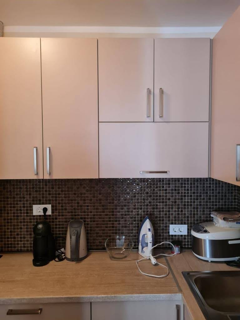 Kitchen in an apartment in Petrovac, Montenegro: light cabinet fronts, a dark mosaic backsplash, and built-in appliances.