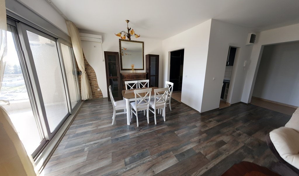 Bright living room with dining area in an apartment in Budva, Montenegro: panoramic windows, wooden floor, and stylish furniture.