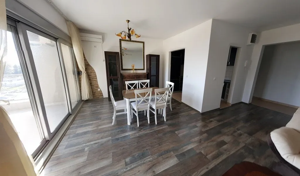 Living room with dining area, white chairs, mirror, and large sliding glass door to balcony.