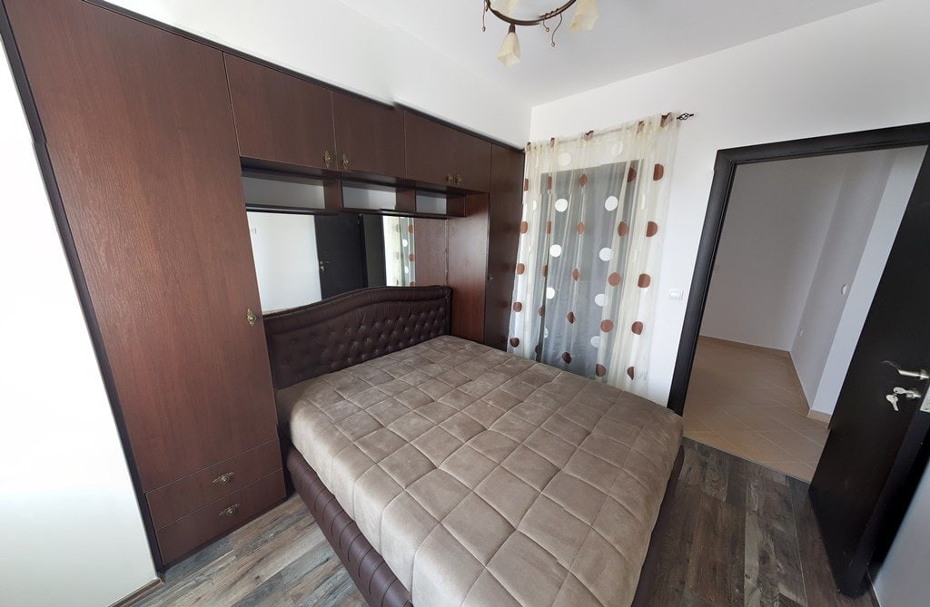 Bedroom with a double bed and built-in wardrobe in an apartment, Budva, Montenegro. Bright interior with dark furniture.