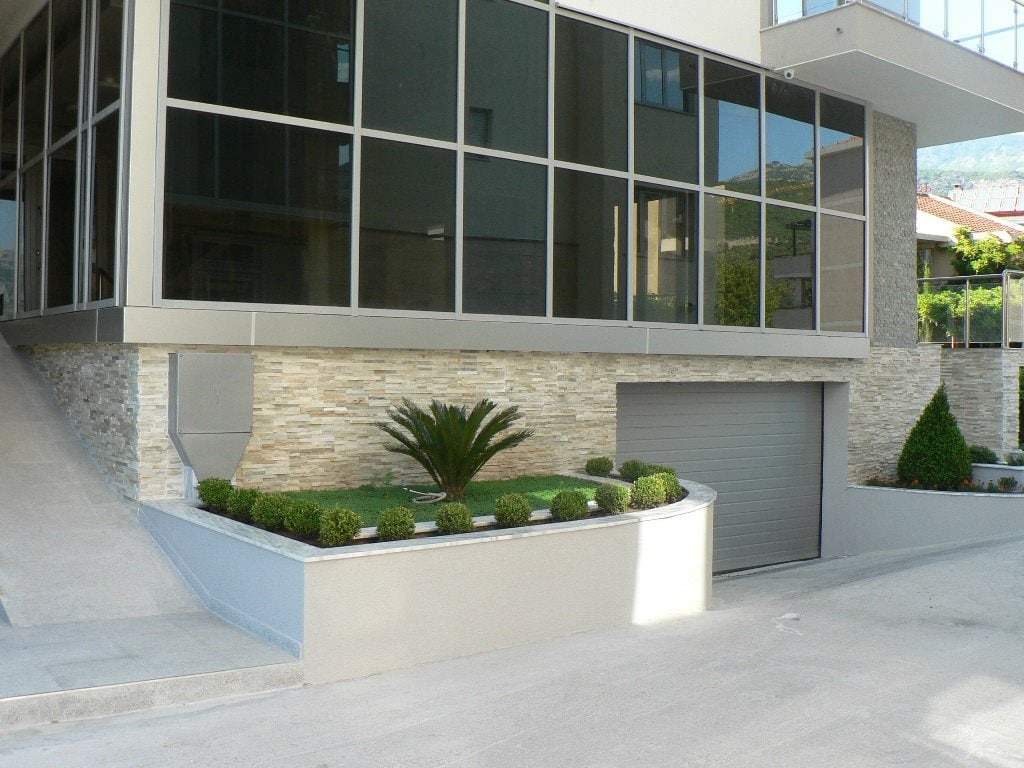 Modern residential house in Budva, Montenegro: panoramic glazing, stone finish, and a private garage with landscaping.