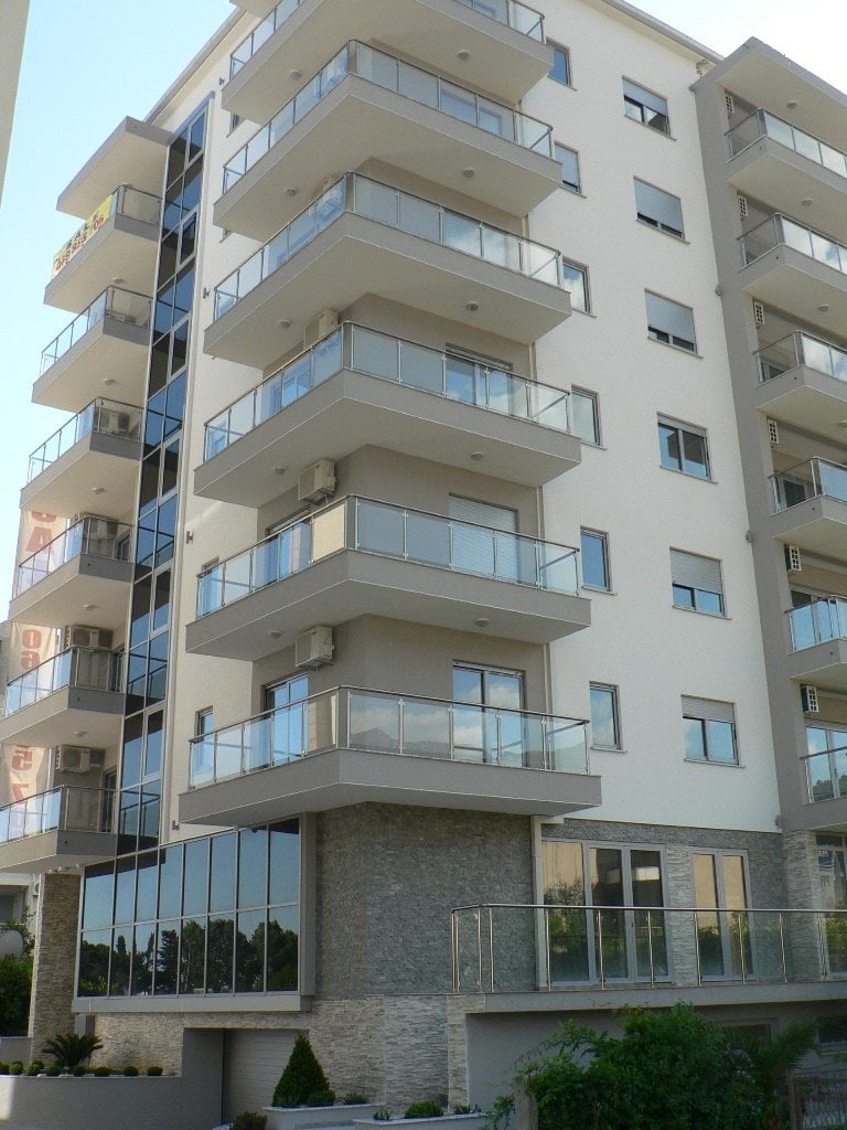 Modern residential building in Budva, Montenegro: facade with panoramic windows, glass balconies, and stone cladding.