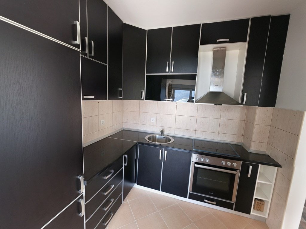 Modern black kitchen with built-in appliances in an apartment, Budva, Montenegro. Corner cabinetry, light tiles.