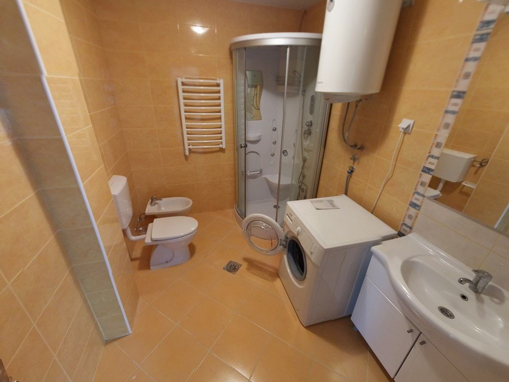 Bathroom in an apartment in Budva, Montenegro: shower cabin, washing machine, bidet, and light-colored tiles.