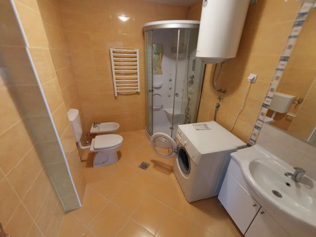 Bathroom with toilet, shower cabin, sink, and washing machine on orange tiles.