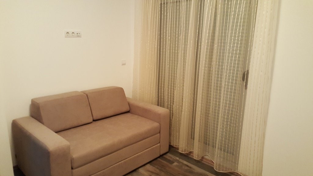 Cozy living room with a beige sofa and a panoramic window in an apartment in Budva, Montenegro. Bright interior with laminate flooring.