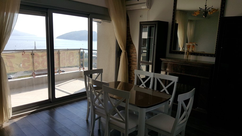 Living room with dining area and panoramic sea view in an apartment in Budva, Montenegro: light furniture and terrace.