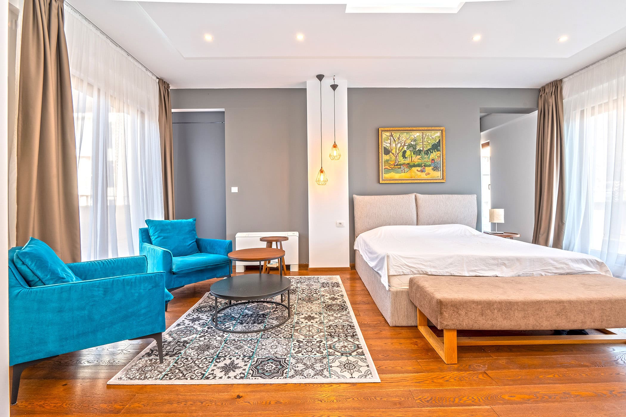 Modern bedroom in an apartment in Budva, Montenegro: double bed, blue armchairs, parquet flooring, and panoramic windows.