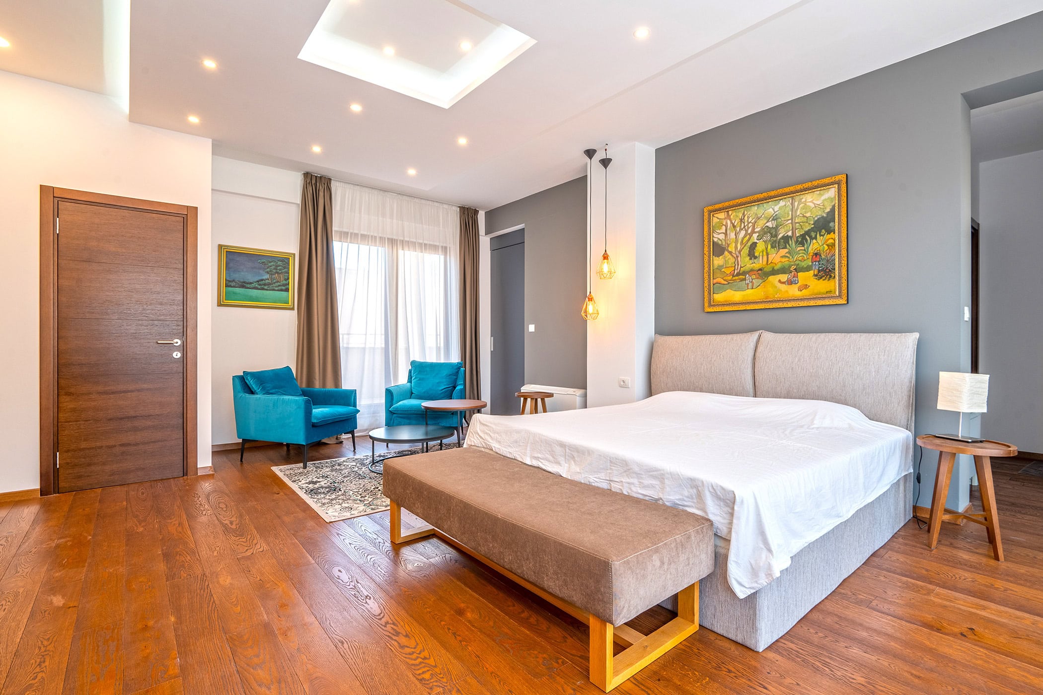 Modern bedroom in an apartment in Budva, Montenegro: a double bed, blue armchairs, wooden floor, and stylish decor.