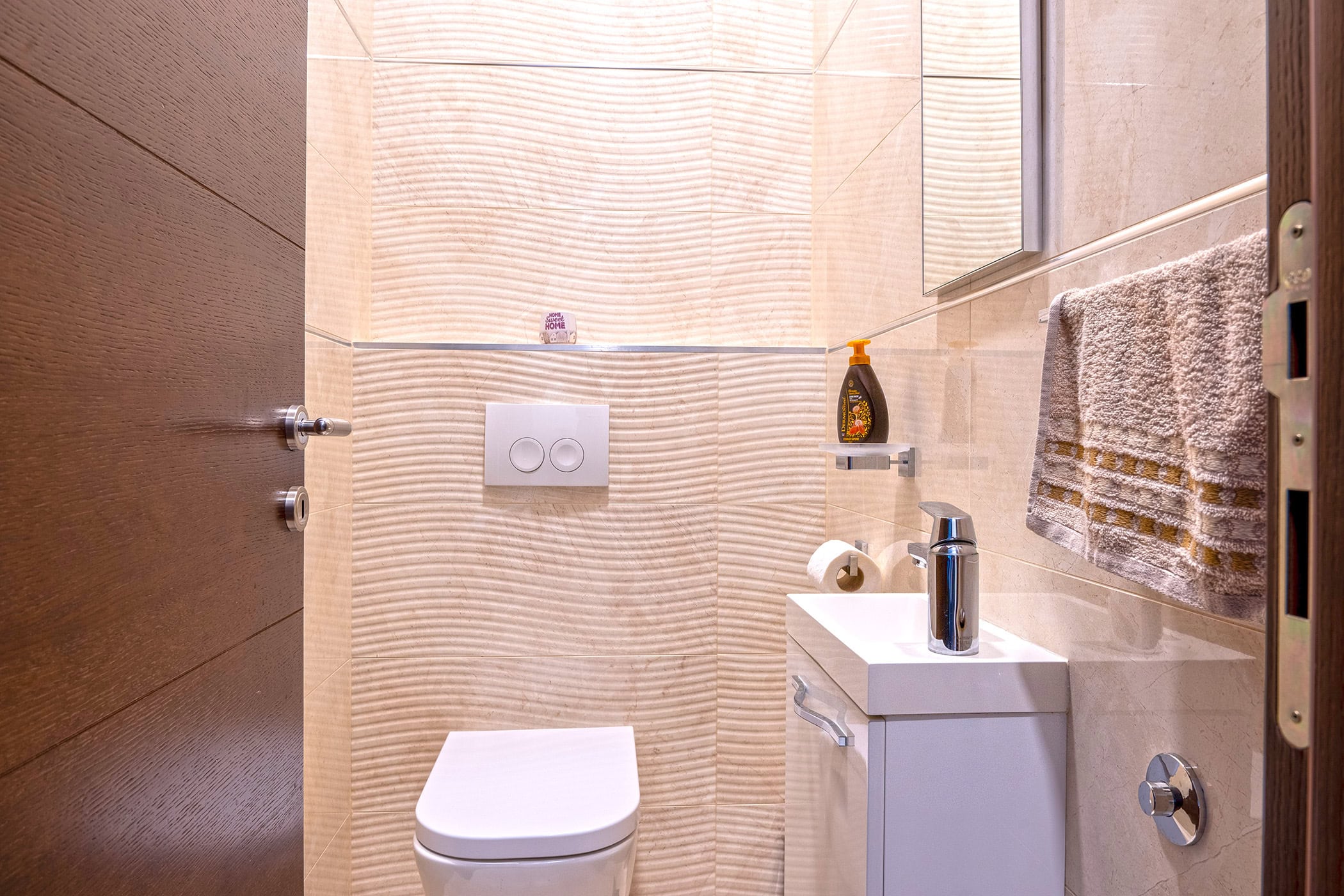Modern bathroom with a wall-mounted toilet and sink in an apartment in Budva, Montenegro, finished with beige tiles.