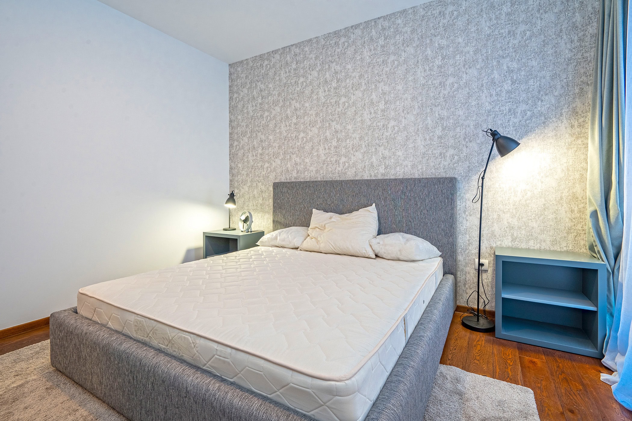 Modern bedroom in an apartment in Budva, Montenegro: double bed, gray nightstands, floor lamp, and accent wall.