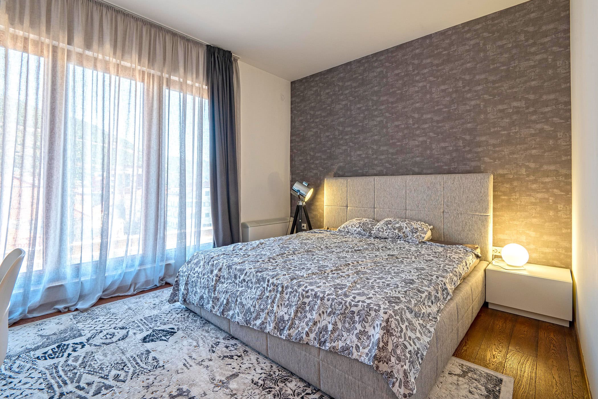 Modern bedroom with a double bed in an apartment in Budva, Montenegro: panoramic window, stylish decor, and lighting.