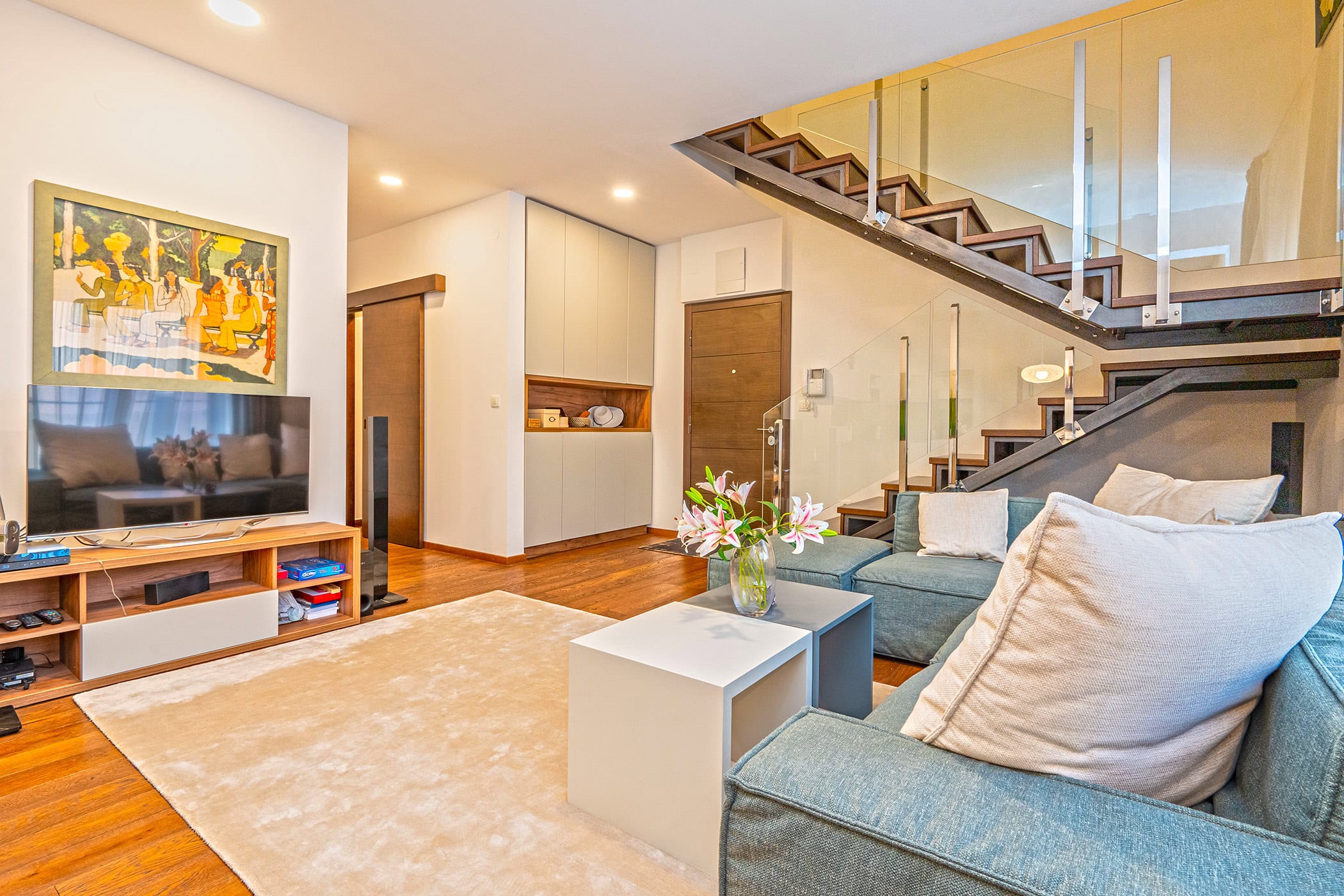 Living room in a duplex in Budva, Montenegro: modern furniture, a light-colored sofa, and a stylish glass staircase.