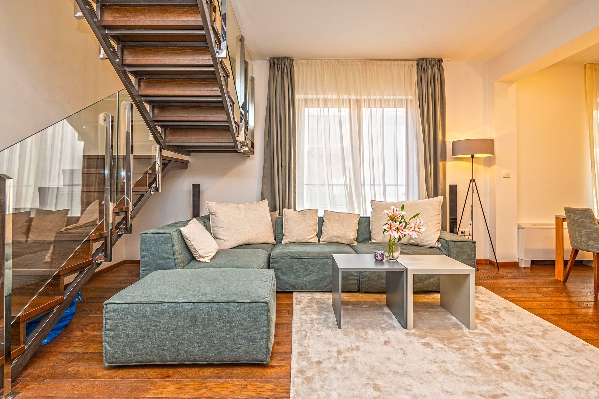 Living room in a duplex in Budva, Montenegro: modern sofa, wooden staircase with glass, and parquet floor.