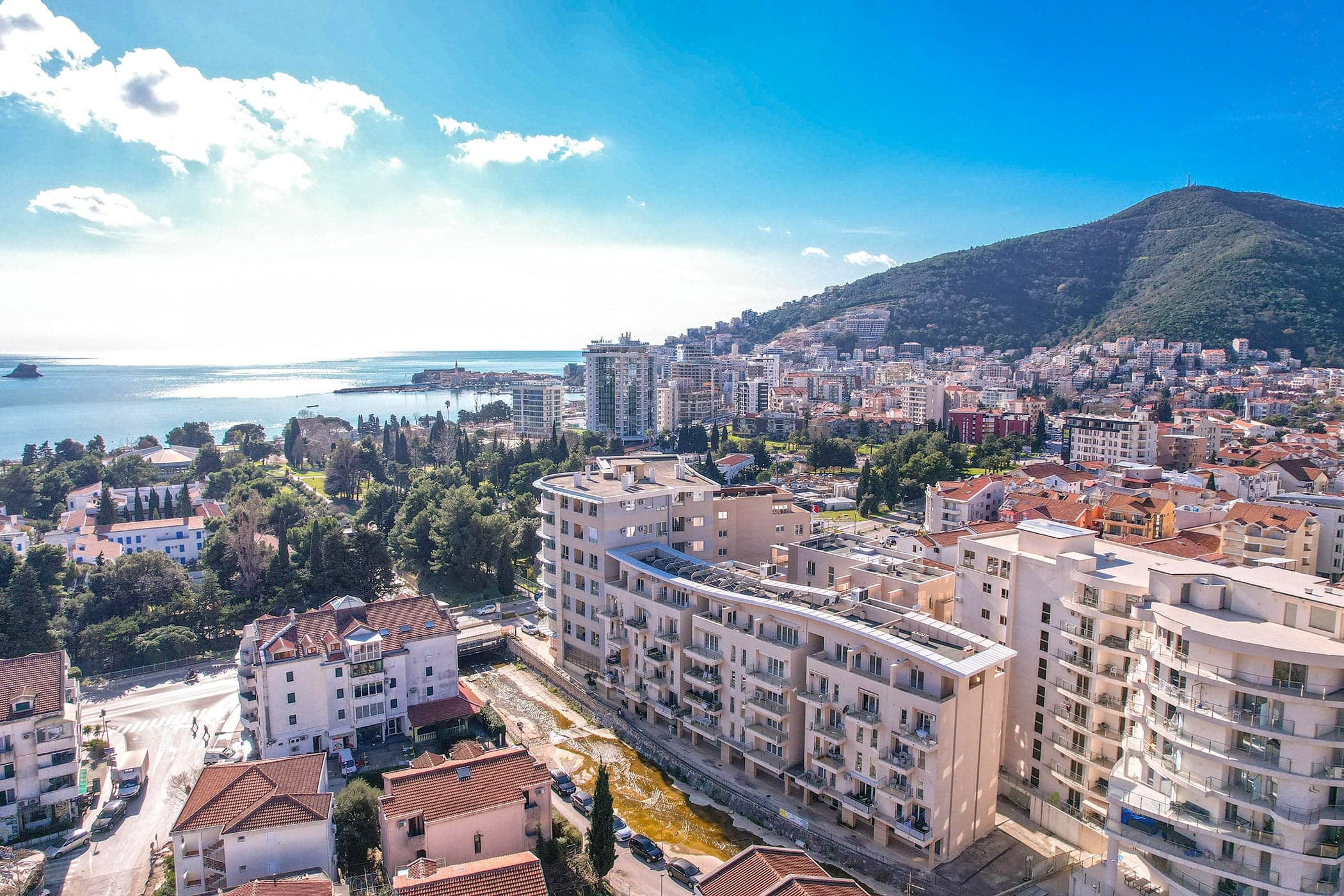 Panoramic view of a residential complex and the Budva coastline, Montenegro: modern architecture, mountains, and the Adriatic Sea.