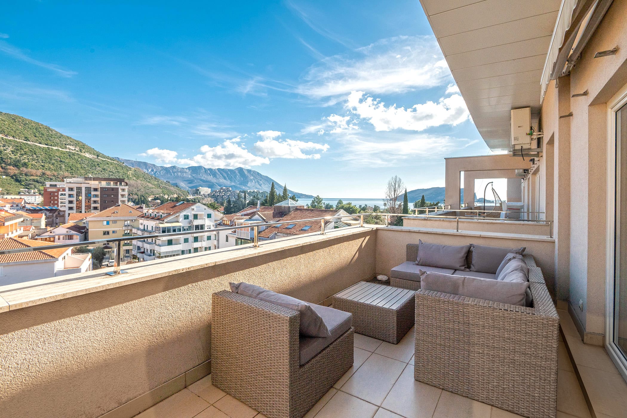 Terrace with wicker furniture and panoramic sea and mountain views in an apartment, Budva, Montenegro.