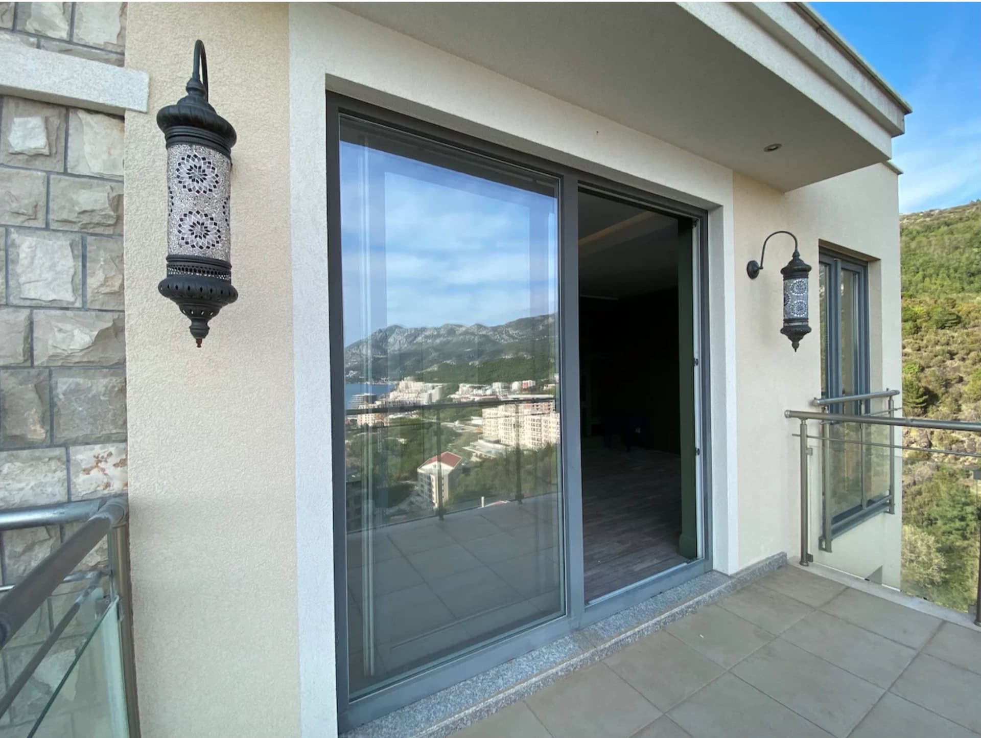 Balcony with panoramic mountain and sea views in an apartment, Becici, Montenegro: stylish wall lights and glazing.