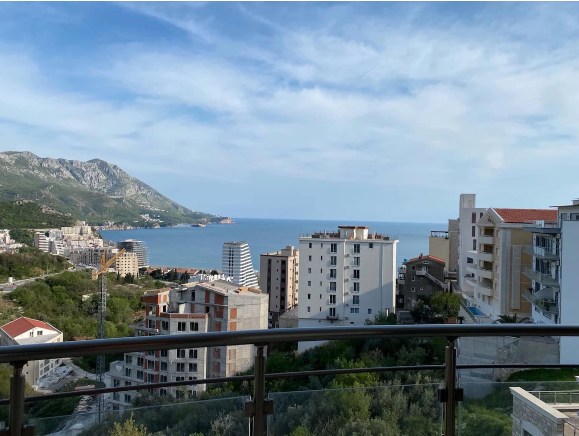 Panoramic sea and mountain view from the apartment balcony in Bečići, Montenegro, overlooking the city buildings and coastline.