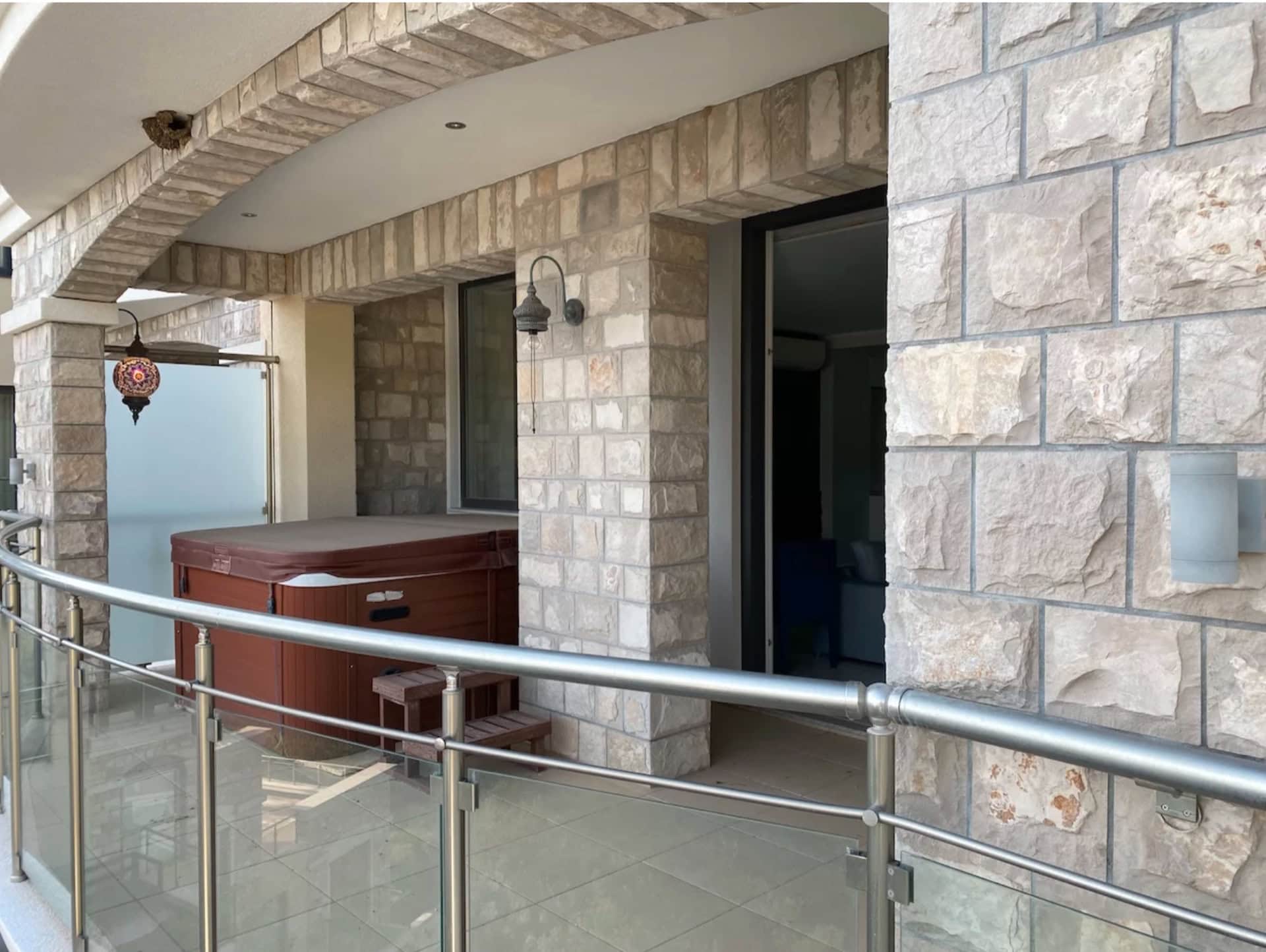 Terrace with a jacuzzi in an apartment in Bečići, Montenegro: natural stone finishes, glass railing, and decor.