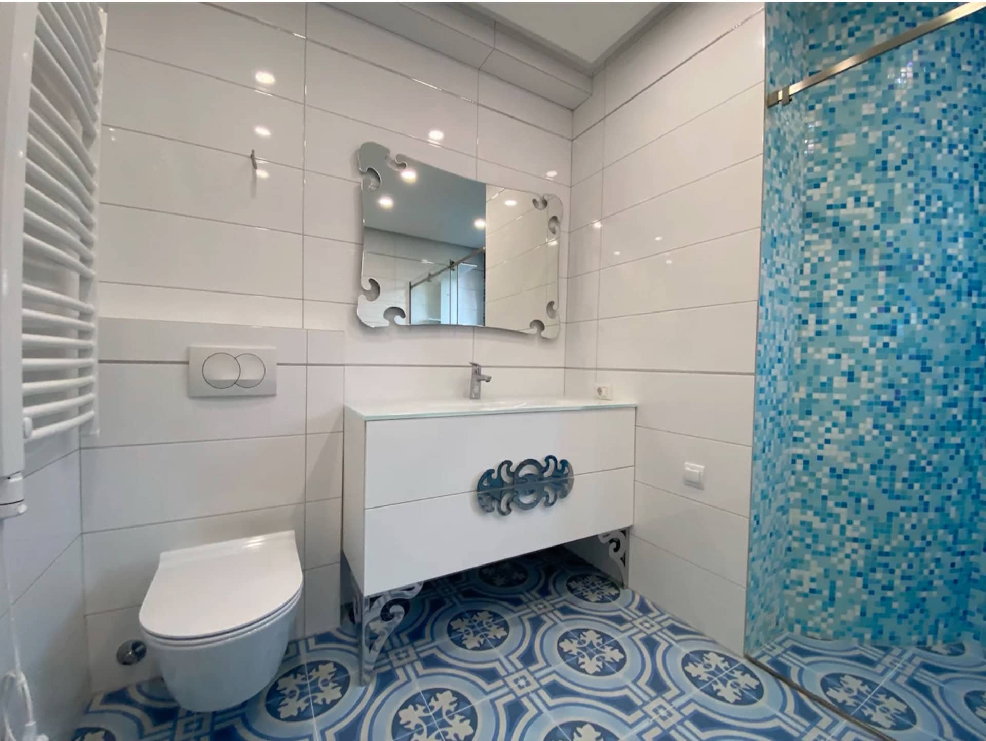 Modern bathroom in an apartment in Bečići, Montenegro: white tiles, a shower with blue mosaic, and patterned flooring.