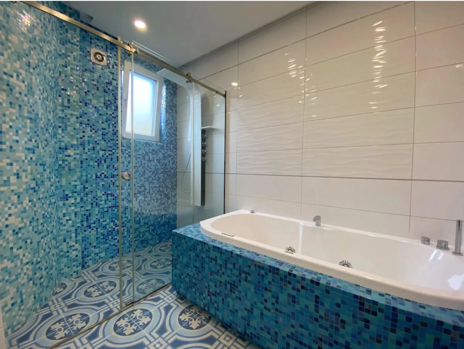 Bathroom with blue mosaic tiles, glass shower enclosure, and white bathtub on a tiled platform.