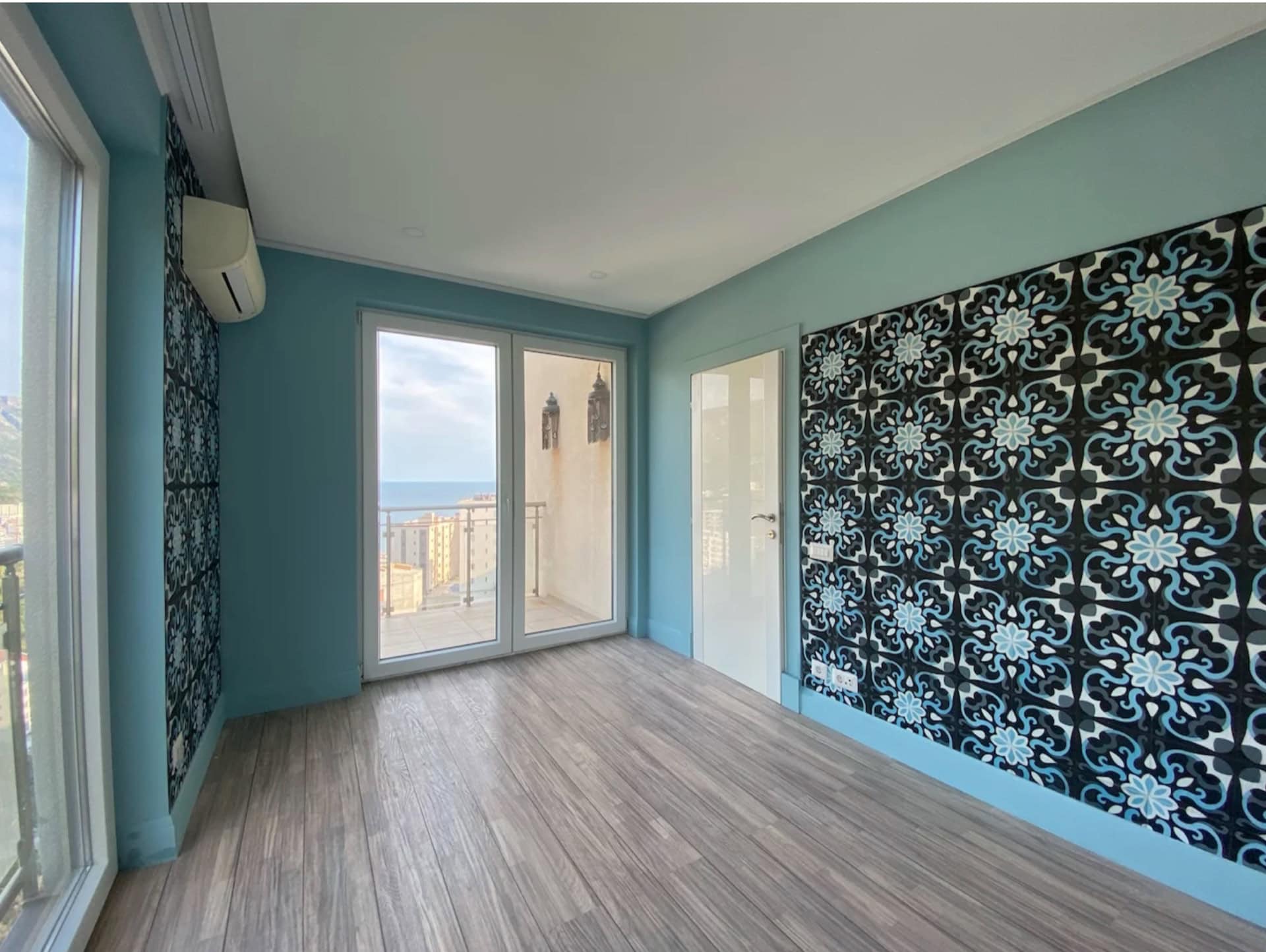 Bright living room in an apartment in Bečići, Montenegro: panoramic windows, sea view, stylish wallpaper, and laminate flooring.