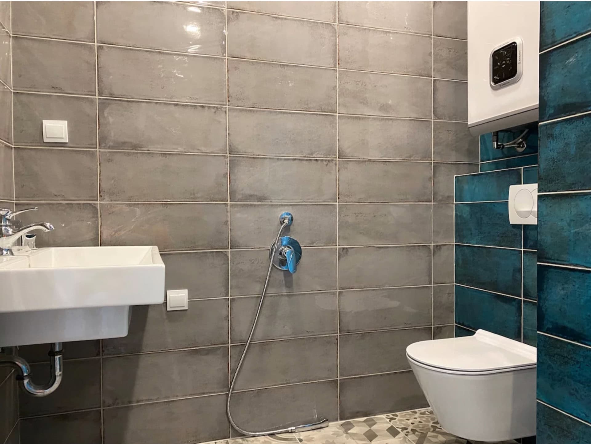 Modern bathroom in an apartment, Becici, Montenegro: gray tiles, wall-mounted toilet, bidet shower, and water heater.