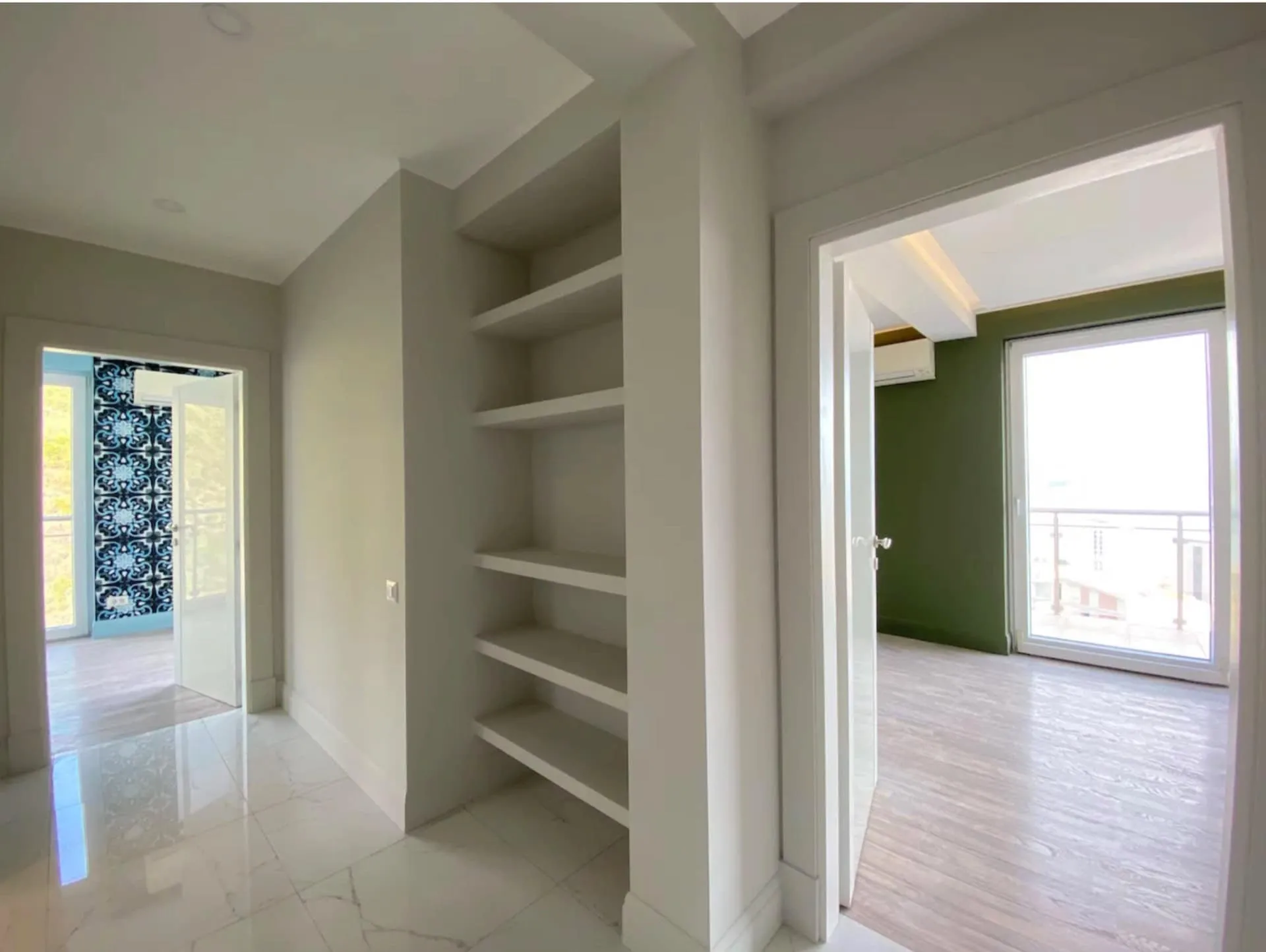 Hallway with built-in white shelves, glossy tile flooring, and doorways leading to adjacent rooms with wood floors.