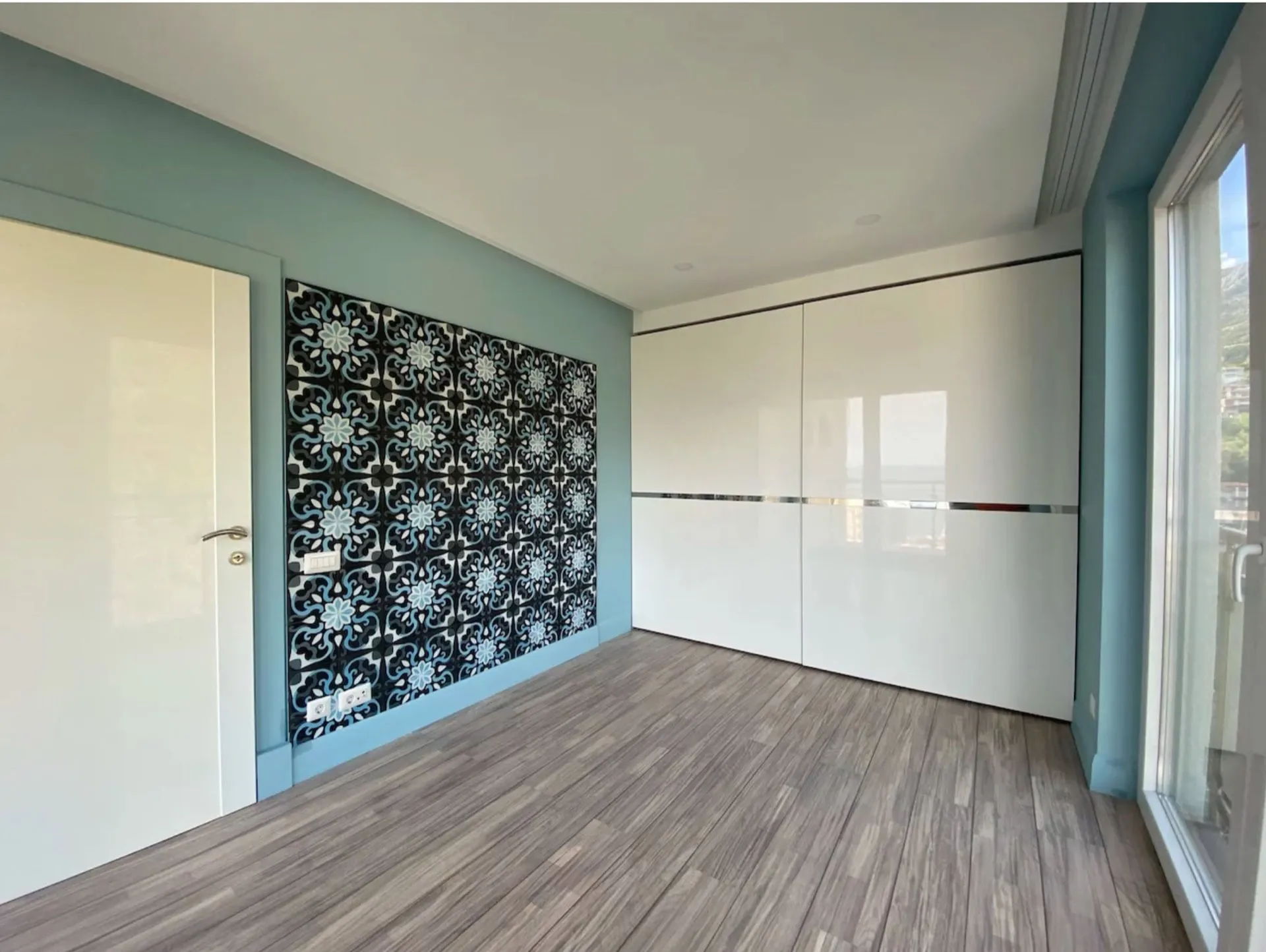 Empty room with white sliding wardrobes and a decorative wall featuring black and blue patterns.