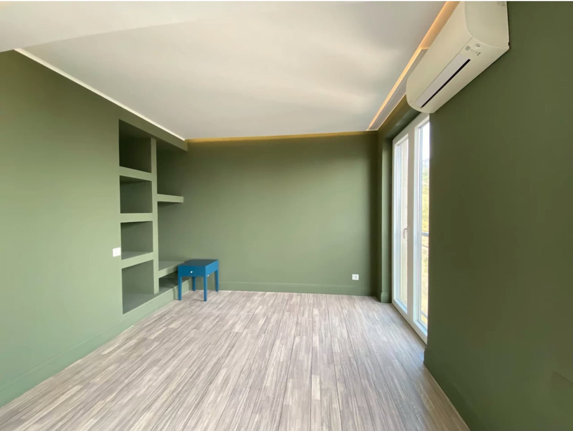 Bedroom in an apartment in Bečići, Montenegro: olive walls, built-in shelves, light flooring, and access to the balcony.