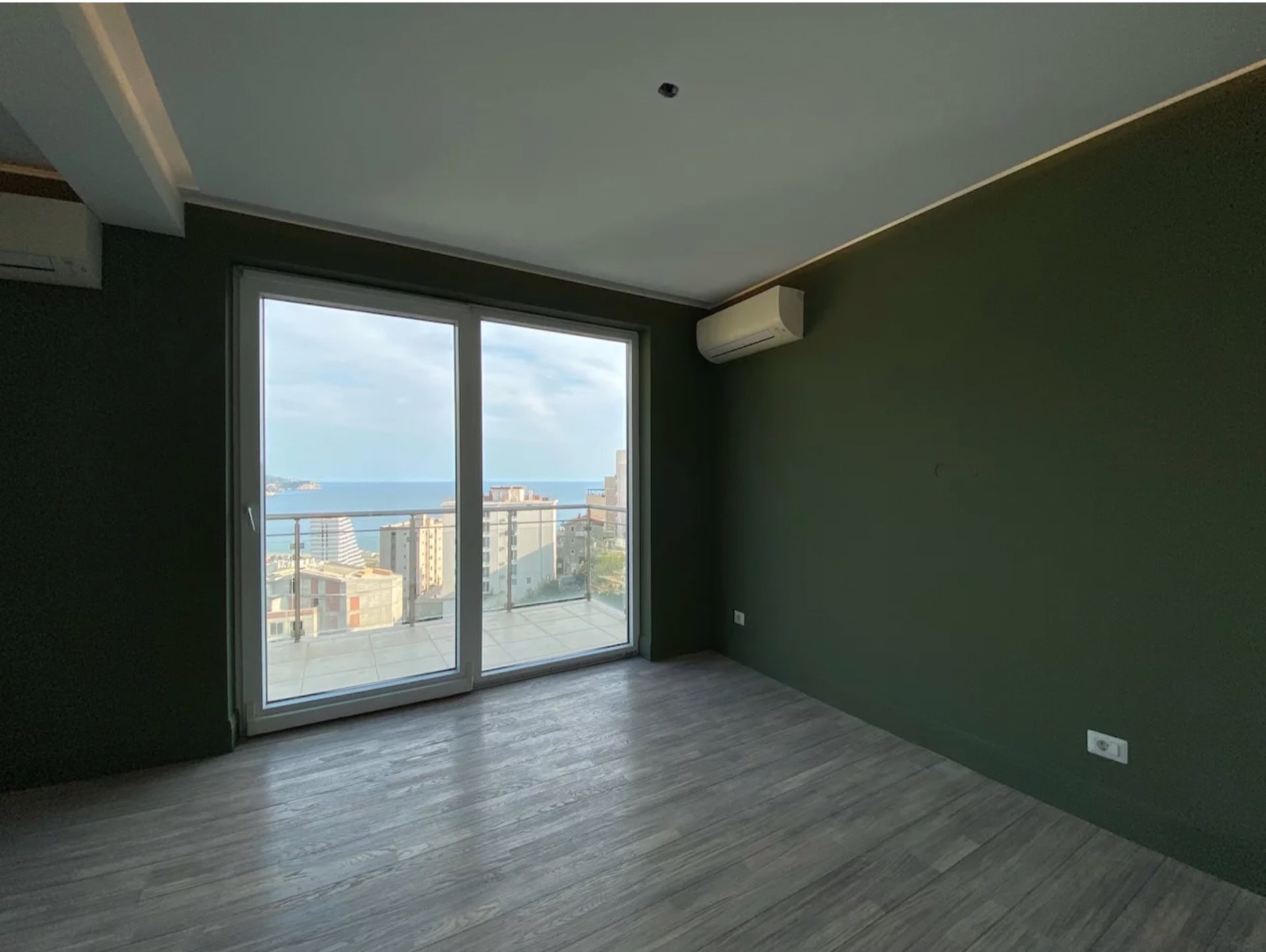 Living room with panoramic sea view in an apartment in Bečići, Montenegro: green walls, light laminate flooring, and a terrace.