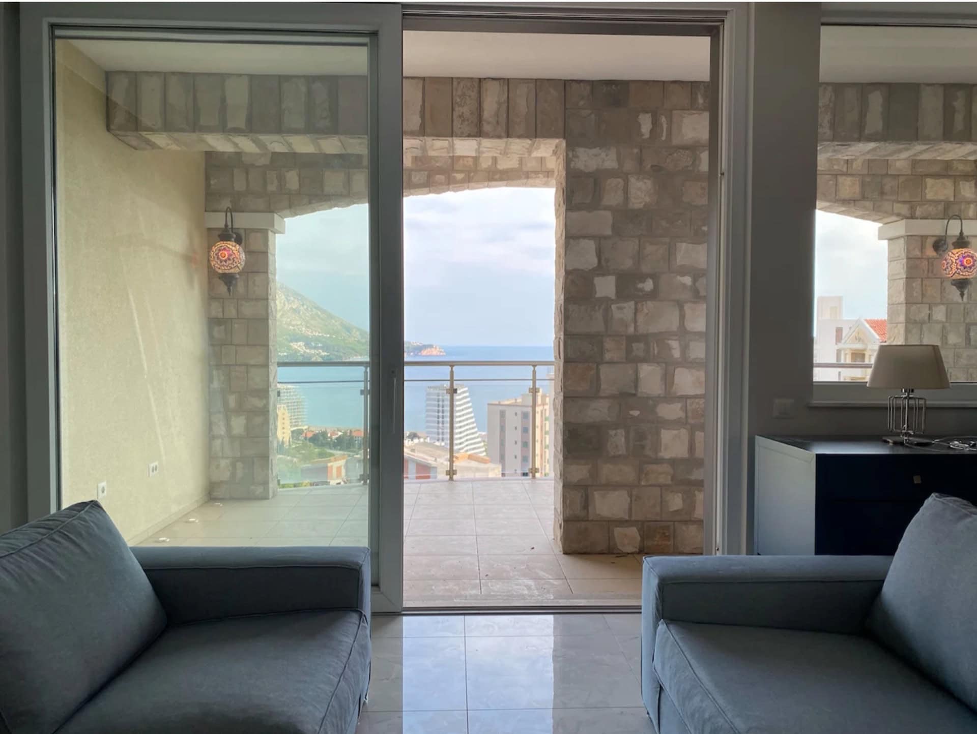 Living room with panoramic sea and mountain views in an apartment, Becici, Montenegro: terrace with stone finishes and sofas.