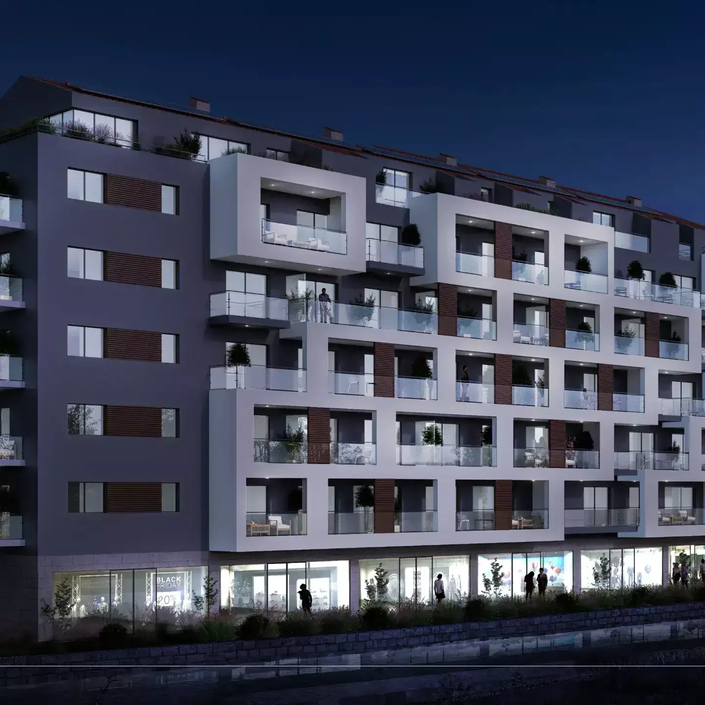 Night exterior view of a modern apartment building with balconies and illuminated ground-floor shops.