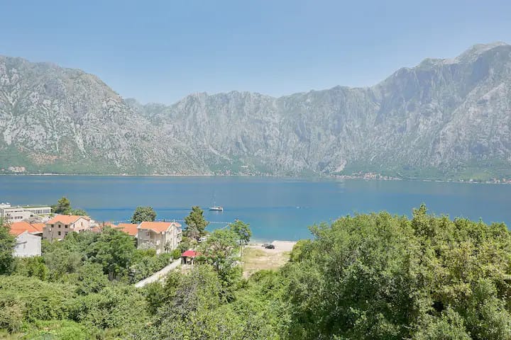 Panoramic view of Kotor Bay and the mountains from an apartment in Prčanj, Montenegro: the sea, yachts, and a green coastal area.