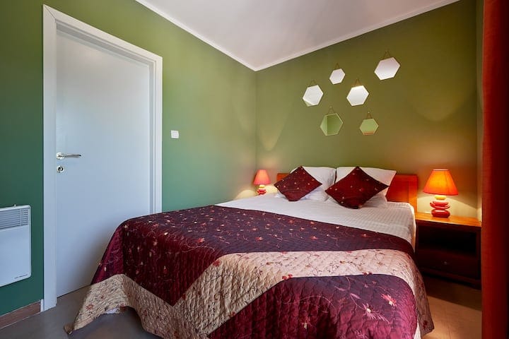 Cozy bedroom with a double bed in an apartment in Prčanj, Montenegro: green walls, mirror decor, and warm lighting.