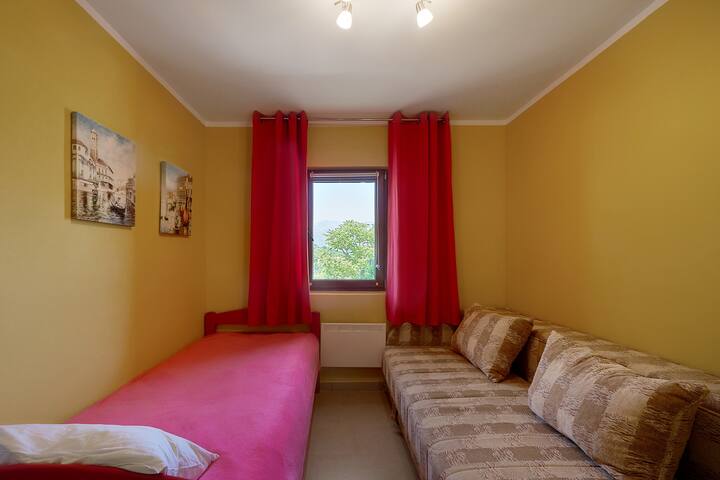 Bedroom in an apartment in Prčanj, Montenegro: two beds, yellow walls, red curtains, and a mountain view from the window.