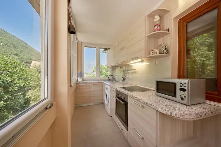 Bright kitchen in an apartment in Prčanj, Montenegro: built-in appliances, stone-look countertop, and mountain view from the window.