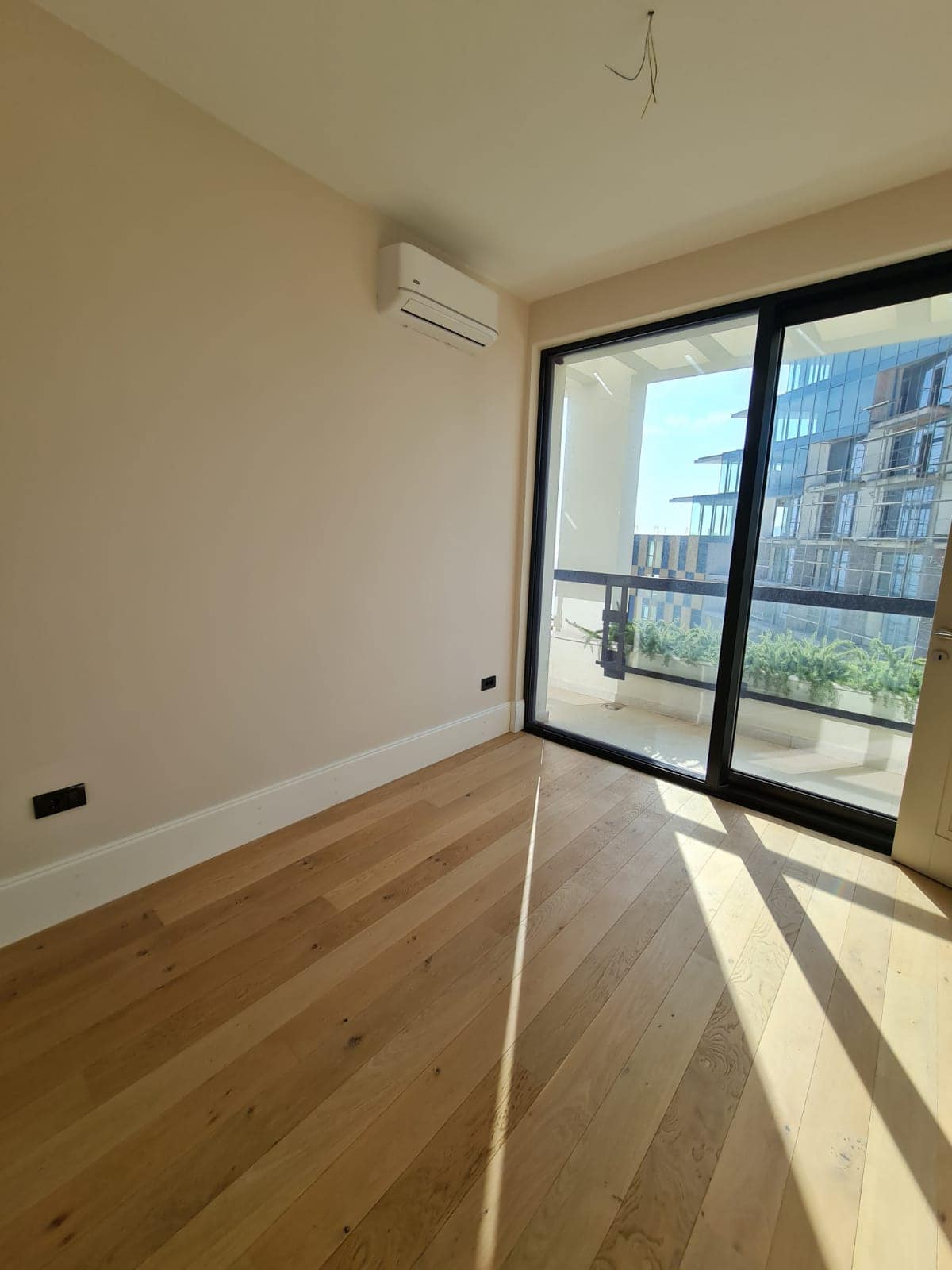 Bright bedroom with parquet flooring, air conditioning, and a panoramic window overlooking the terrace in an apartment, Rafailovici, Montenegro.
