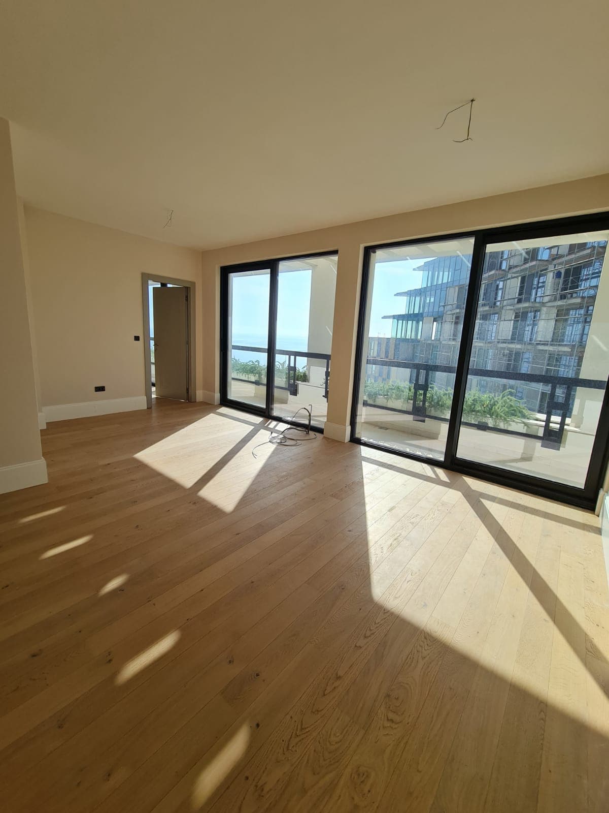 Bright living room in a new building in Rafailovici, Montenegro: panoramic windows, sea view, and parquet flooring, unfurnished.