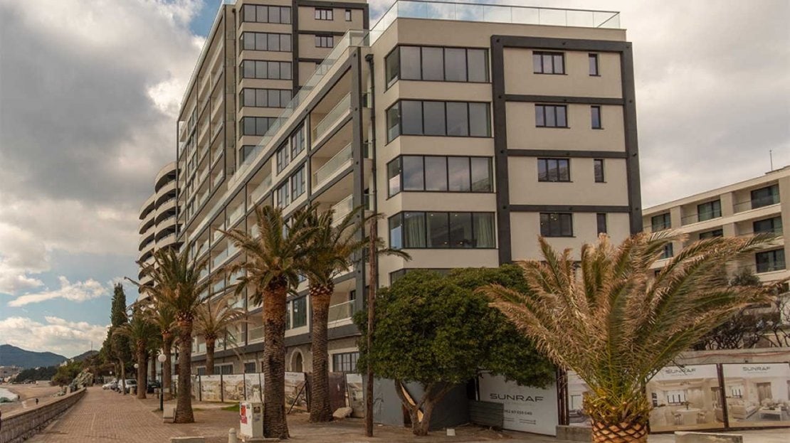 Modern residential complex by the sea in Bečići, Montenegro: panoramic windows, balconies, and palm trees on the promenade.