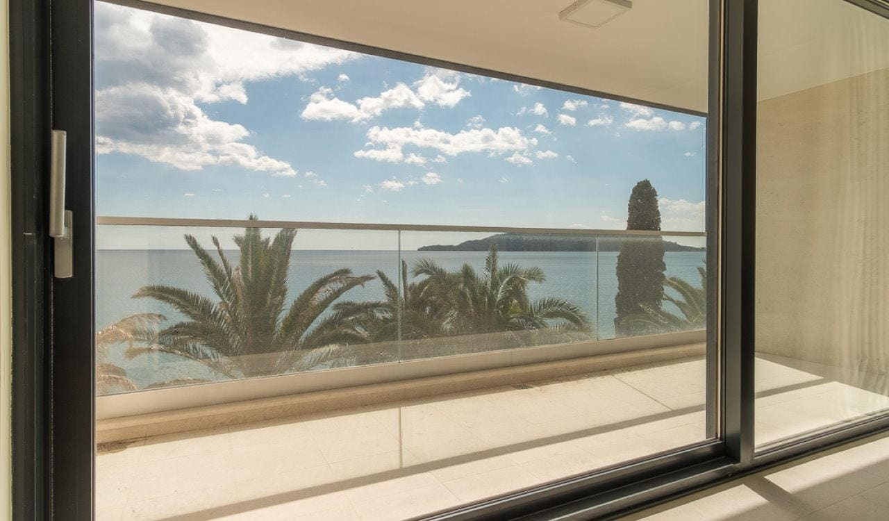 Sea and palm trees view from the spacious balcony of the apartment in Bečići, Montenegro, with panoramic glazing.